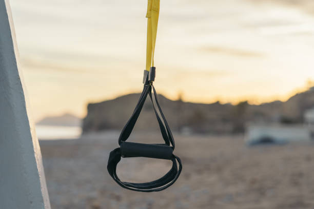Suspended fitness webbing system hanging outdoors on the beach at sunset.