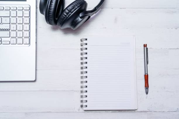A blank notebook with a pen on an office table with a laptop and headphones.
