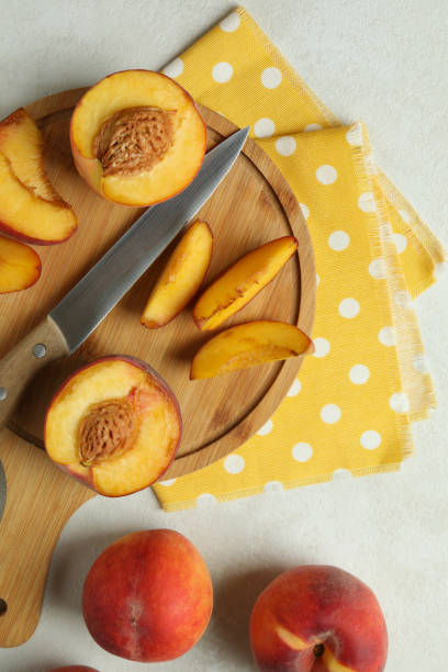 istock Board with peach fruits, knife and kitchen towel on white textured table 1481606810