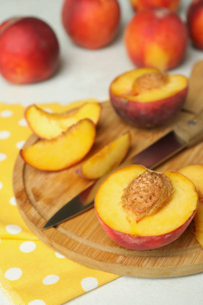 istock Board with peach fruits, knife and kitchen towel on white textured table 1481608147