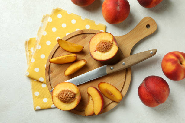 istock Board with peach fruits, knife and kitchen towel on white textured table 1481608417
