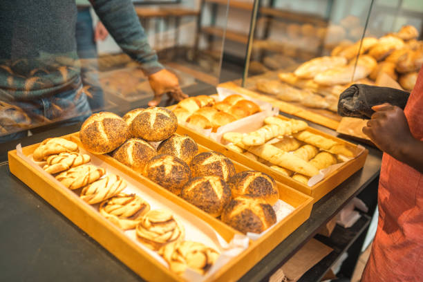 Close up on hands of Black female shop assistant handling an order in a small artisan bakery. Putting items in a paper bag.