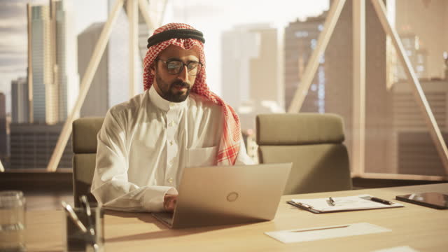 Portrait of a Young Saudi Business Account Manager Working on a Laptop Computer in a Modern Corporate Office. Businessman Dealing with Financial Reports, Preparing a Growth Plan for the Company