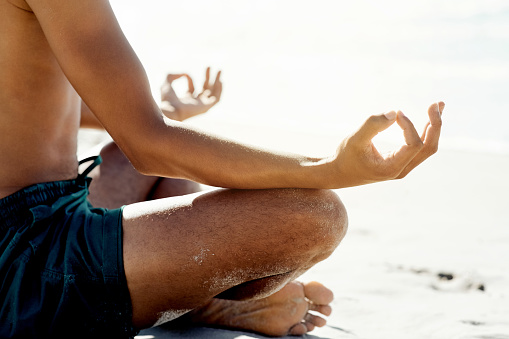 Hands, zen and meditation with a man on the beach, sitting legs crossed for wellness on the sand by the ocean. Yoga, balance and inner peace with a male meditating near the sea for mental health