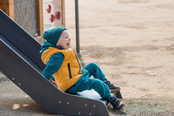 un niño pequeño camina por el patio de recreo en la primavera. el niño se está divirtiendo bajando la colina. infancia y desarrollo infantil. - 2 3 months beginnings new life caucasian fotografías e imágenes de stock