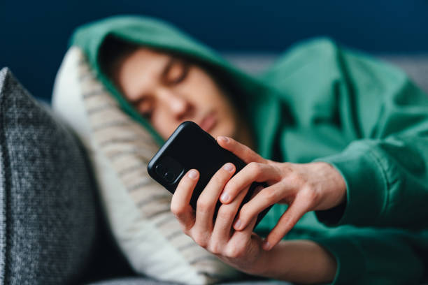 Close Up Photo Of Teenager Hands Using A Mobile Phone At Home An anonymous teenage boy typing text messages on his smartphone while lying on a couch at home. online bullying stock pictures, royalty-free photos & images