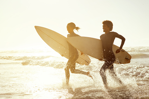 Sunset, running and couple on the beach with surfboards to practice surfing while on vacation. Nature, sports and young man and woman surfers in the ocean or sea while on a tropical holiday in Hawaii