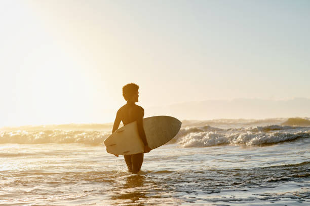 istock Sunset, beach and man with a surfboard in the ocean for training while on holiday or vacation. Water sport, travel and male surfer practicing surfing in sea while on tropical weekend trip by twilight 1481614627