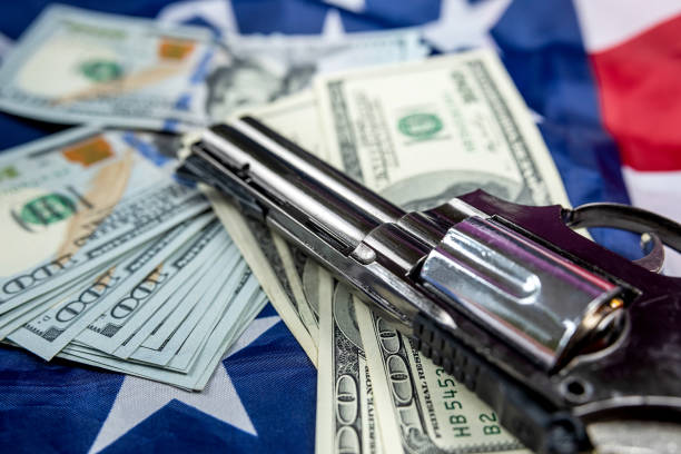 vue de dessus d’un gros pistolet noir et d’un tas de dollars américains sur un grand drapeau américain spacieux. - currency crime gun conflict photos et images de collection