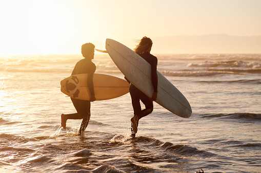 Men, surfer friends and running at sunset beach for waves, freedom and swim from behind. Silhouette, surfing and guys with board at sea, sunshine and adventure on holiday, summer and fun water sports