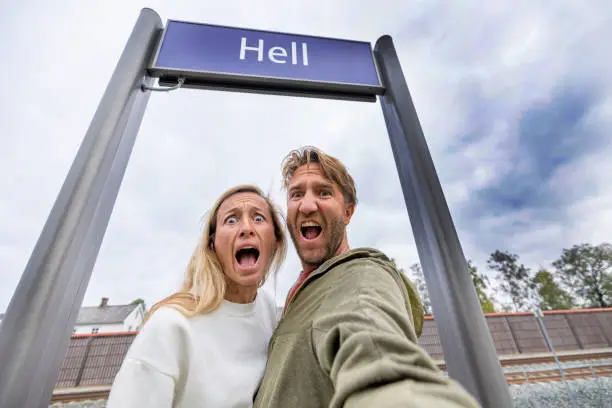 Photo of A couple making a face under the Hell sign at the railroad station, Norway, they take a selfie