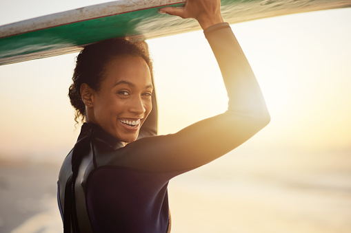 Happy, surfer or portrait of woman at sea for fitness training, workout or sports exercise at sunset. Surfing, surfboard or mixed race athlete smiling on fun summer holiday vacation alone on beach