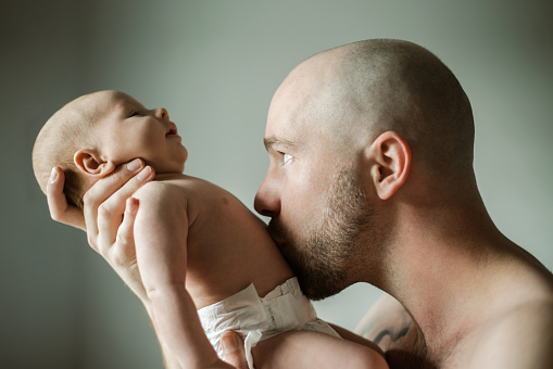 Face, family and baby with a father kissing his child in studio on a gray background for love or care. Kiss, kids or together and a man bonding with his newborn infant through skin contact