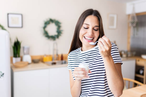 Serene young beautiful woman eating bio yogurt in the kitchen at home stock photo