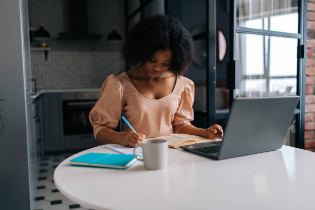 istock Successful African female student brainstorming ideas and writing down on paper notebook in self education sitting at desk with laptop and coffee cup. 1481622704