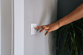 Close-up hands of unrecognizable African American woman turning on light in dark room by pushing switch on white wall.