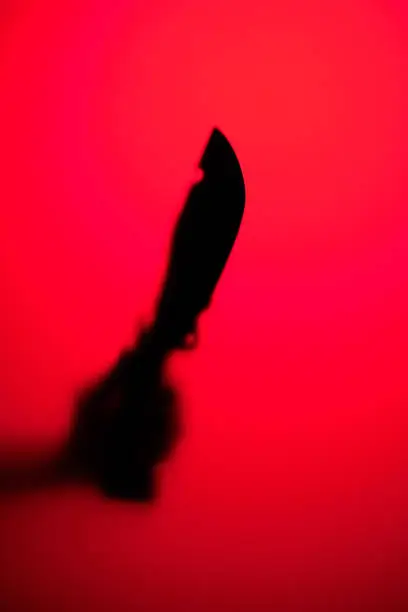 A hand is holding a large knife against a background of red neon light.