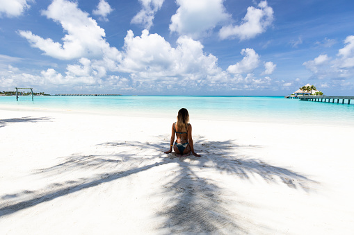 Rear view of a woman sitting in a shadow on the beach and looking at view. Copy space.