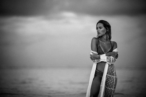 Black and white photography of a beautiful woman standing on the beach and day dreaming. Copy space.