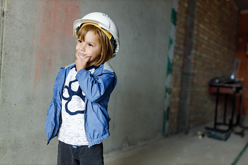 Pensive little manual worker with hardhat brainstorming at construction site. Copy space.