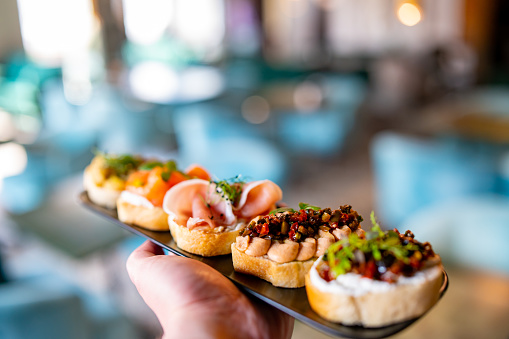 man hand hold various bruschettas with toppings on black plate