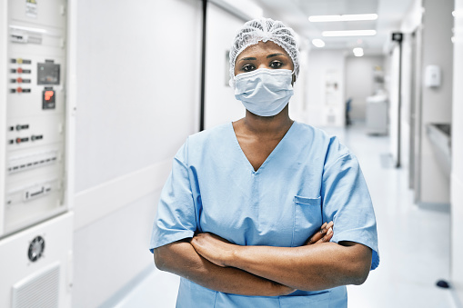 Portrait of a female nurse wearing surgical mask and cap. African woman doctor in uniform standing at hospital corridor.