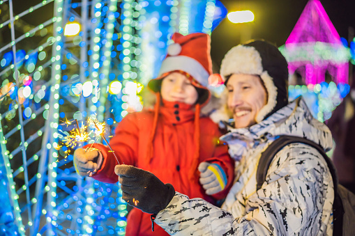 Little boy and his father with sparklers near giant fir tree and Christmas illumination on Christmas market. Xmas holidays on fair.