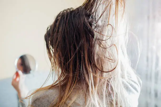 Photo of Close up of woman touching dirty oily and greasy hair looking in mirror at home. Time to wash head with shampoo