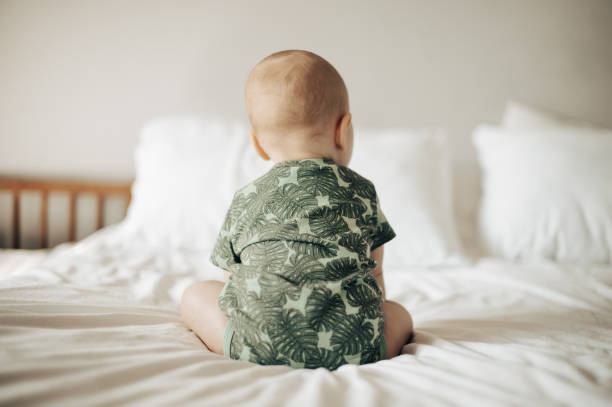 Baby, back view and infant sitting on a bed in a bedroom relax in development in as home or house being cute and curious. Toddler, child or kid in a nursery relaxing enjoying childhood and playing stock photo
