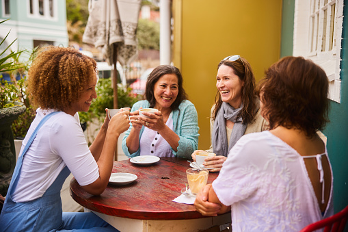 Smiling group of mature female friends talking and laughing over coffee together at table outside at a sidewalk cafe