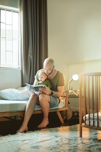 Family, dad with baby and reading book with learning, storytelling and development in bedroom with growth. Man, kid and education, bonding and love with care, learn language and early childhood