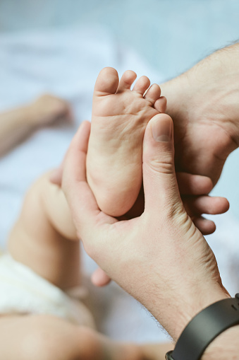 Small, care and parent showing baby feet, newborn human and love for parenthood. Family, cute and hand of a father holding a foot of a child for loving, tenderness and youth in the bedroom of a house