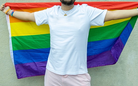 A young man stands proudly with a rainbow-colored flag draped over his shoulders