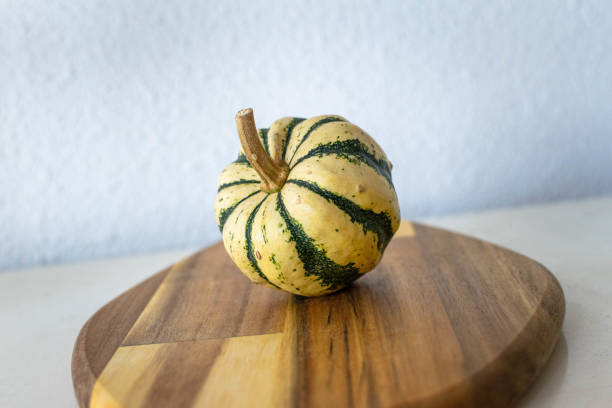 Isolated decorative round mini pumpkin A single round decorative mini pumpkin isolated on a wooden chopping board miniature pumpkin stock pictures, royalty-free photos & images