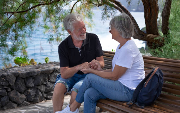 istock Romantic senior couple hands in hands sitting outdoor on a bench under a tree looking into each other eyes smiling. Support, love, tenderness in retirement couple 1481642296
