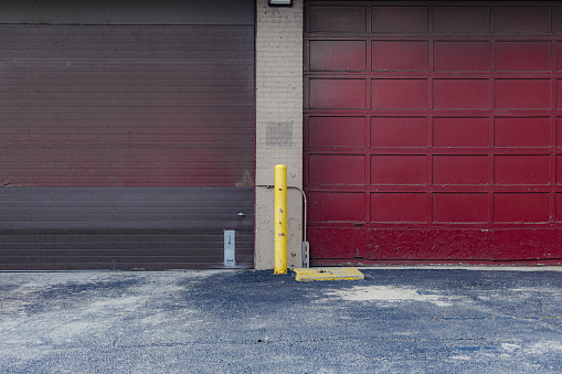 Two large red industrial garage doors and tired pavement in urban Chicago