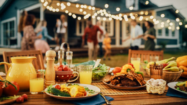 mesa de cena en el patio trasero con sabrosa carne a la parrilla, verduras frescas y ensaladas. gente alegre y feliz bailando al ritmo de la música, celebrando y divirtiéndose en el fondo en el porche de la casa. - barbacoa comida fotografías e imágenes de stock