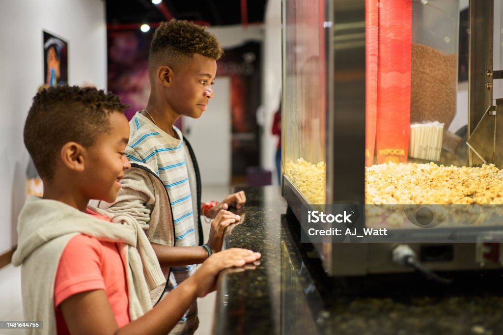 Two Brazilian boys buying popcorn at concession stand in a movie theater Side view of two Brazilian boys standing at concession stand buying popcorn in a movie theater Child Stock Photo