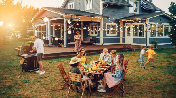 big family and friends celebrating outside at home. diverse group of children, adults and old people gathered at a table, having fun conversations. preparing barbecue and eating vegetables. - tuin feest stockfoto's en -beelden