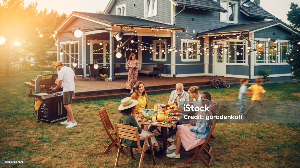 Big Family and Friends Celebrating Outside at Home. Diverse Group of Children, Adults and Old People Gathered at a Table, Having Fun Conversations. Preparing Barbecue and Eating Vegetables. Family Stock Photo