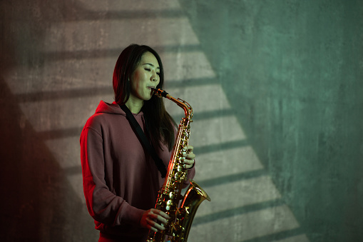 Portrait of a beautiful Japanese female playing saxophone in studio.