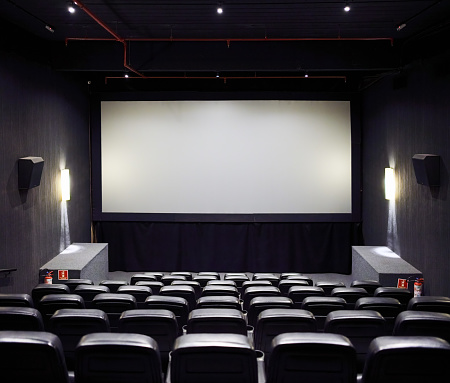 Interior of film theater with empty leather seats and blank white projector screen