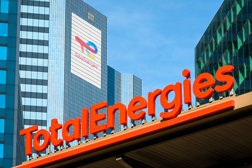 Courbevoie, France - April 9, 2023: Sign of a TotalEnergies service station with the Coupole tower in the background, head office of the oil company in Paris La Defense business district.