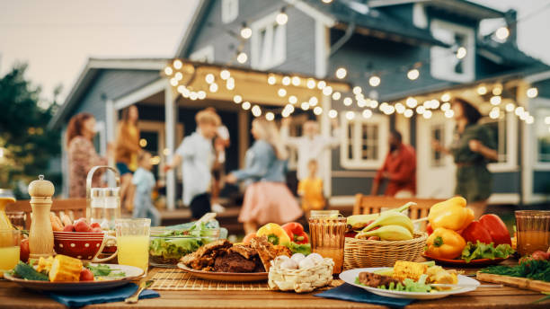 istock Outdoors Dinner Table with Gorgeous-Looking Barbecue Meat, Fresh Vegetables and Salads. Happy Joyful People Dancing to Music, Celebrating and Having Fun in the Background on Home Porch. 1481647713