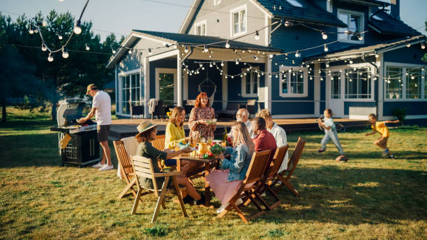 parents, enfants et amis se sont réunis autour d’une table de barbecue à l’extérieur d’une belle maison. les vieux et les jeunes s’amusent, mangent et boivent. fête de jardin dans une cour arrière. - jardin de derrière photos et images de collection
