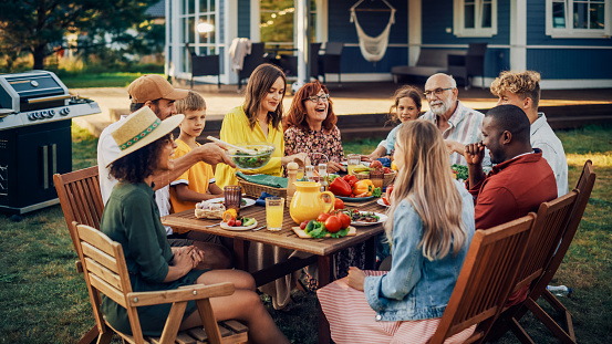 Padres, hijos, parientes y amigos teniendo una cena vegetariana al aire libre en su patio trasero. Los ancianos y los jóvenes hablan, charlan, se divierten, comen y beben. Celebración de la fiesta en el jardín en un patio trasero. photo