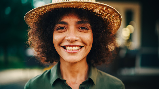 Portrait of a Happy Multiethnic Female Smiling Sincerely, Laughing and Looking at Camera. Young Female with Curly Hair Wearing a Fedora Hat, Posing, Expressing Joy and Positive Attitude.