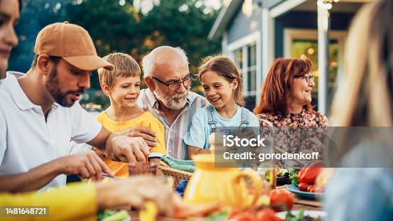 istock Portrait of a Happy Senior Grandfather Holding His Bright Talented Little Grandchildren on Lap at a Outdoors Dinner Party with Food and Drinks. Family Having a Picnic Together with Children. 1481648721