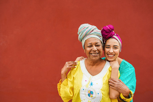 Happy african mother and her daughter wearing ethnic afro clothes while smiling in front of camera - Mom day, family and love concept
