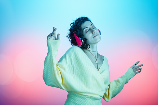 Beautiful young woman enjoying her favorite music against multicolored background